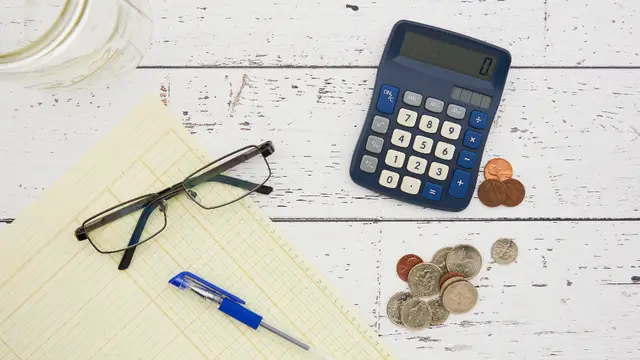 A calculator, glasses and coins on a desk