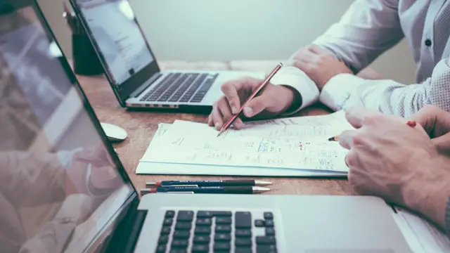Hands going through payslip paperwork beside a laptop