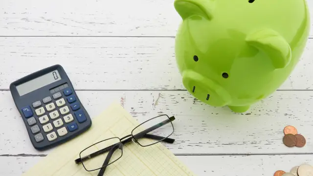 A green piggy bank beside a calculator and glasses